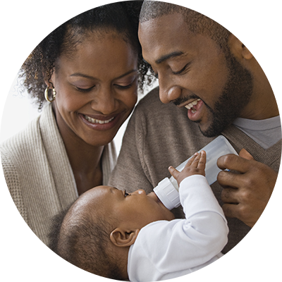 Smiling parents bottlefeed their baby with infant formula milk, confident in the quality formulas they feed him.