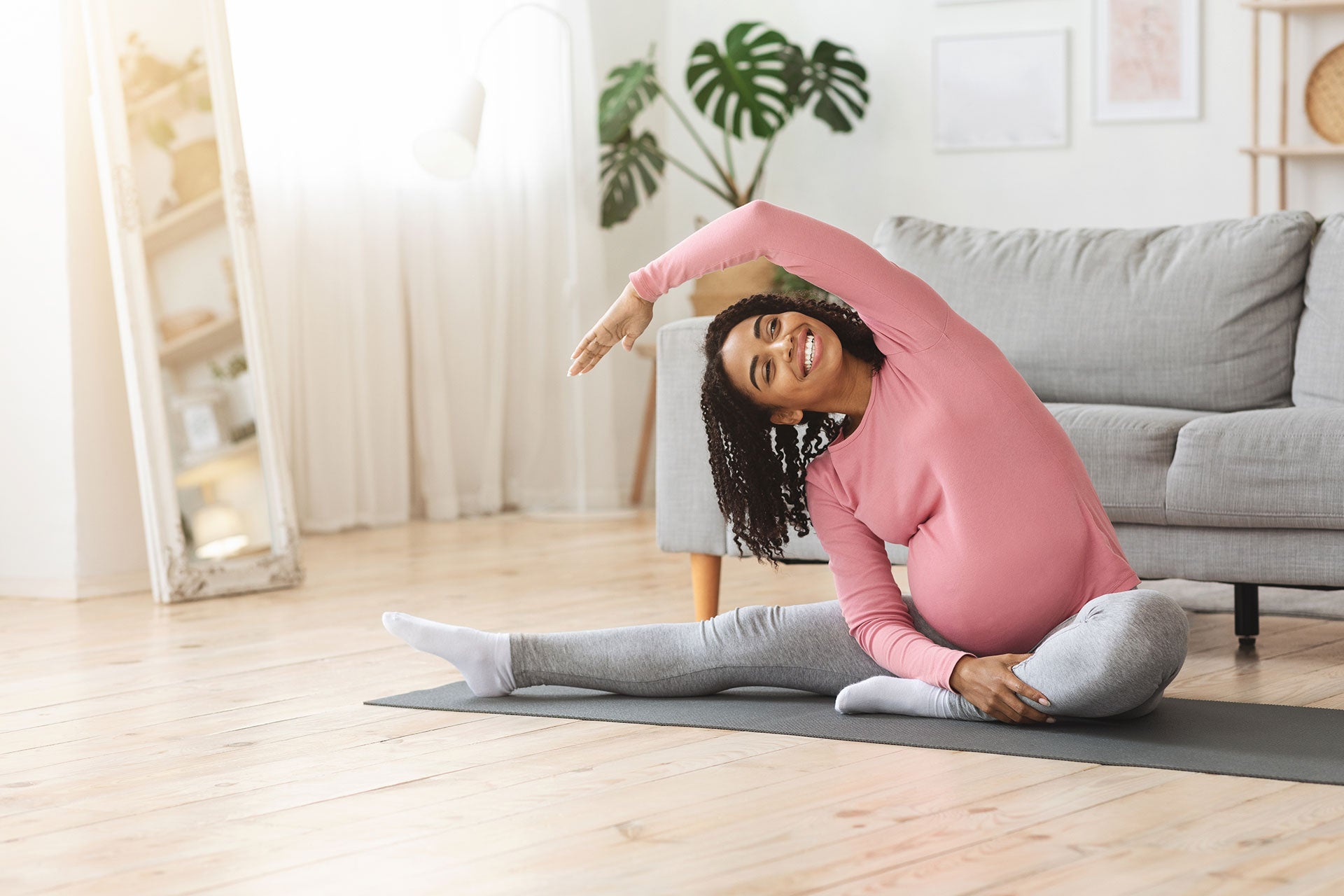 A pregnant woman smiles doing floor yoga, deciding to stay active with prenatal exercise.