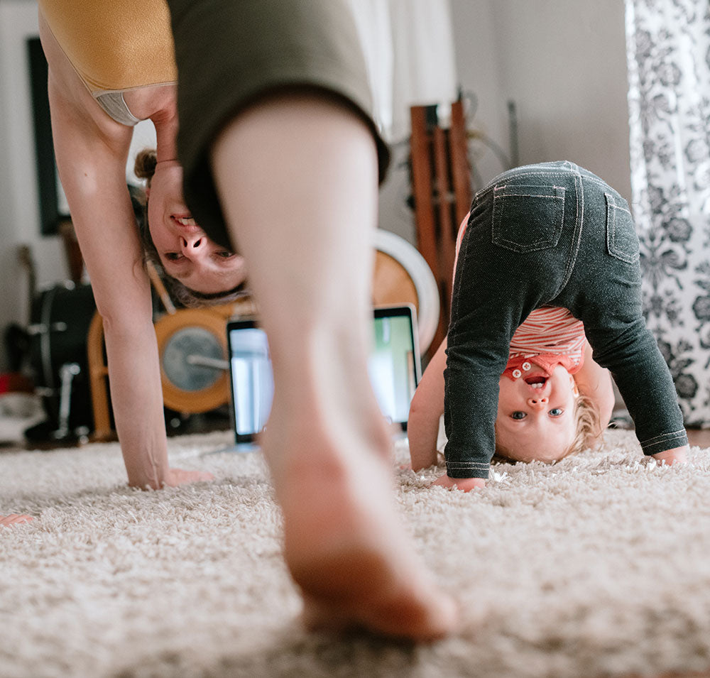 A toddler and mom playfully do yoga together in the living room.