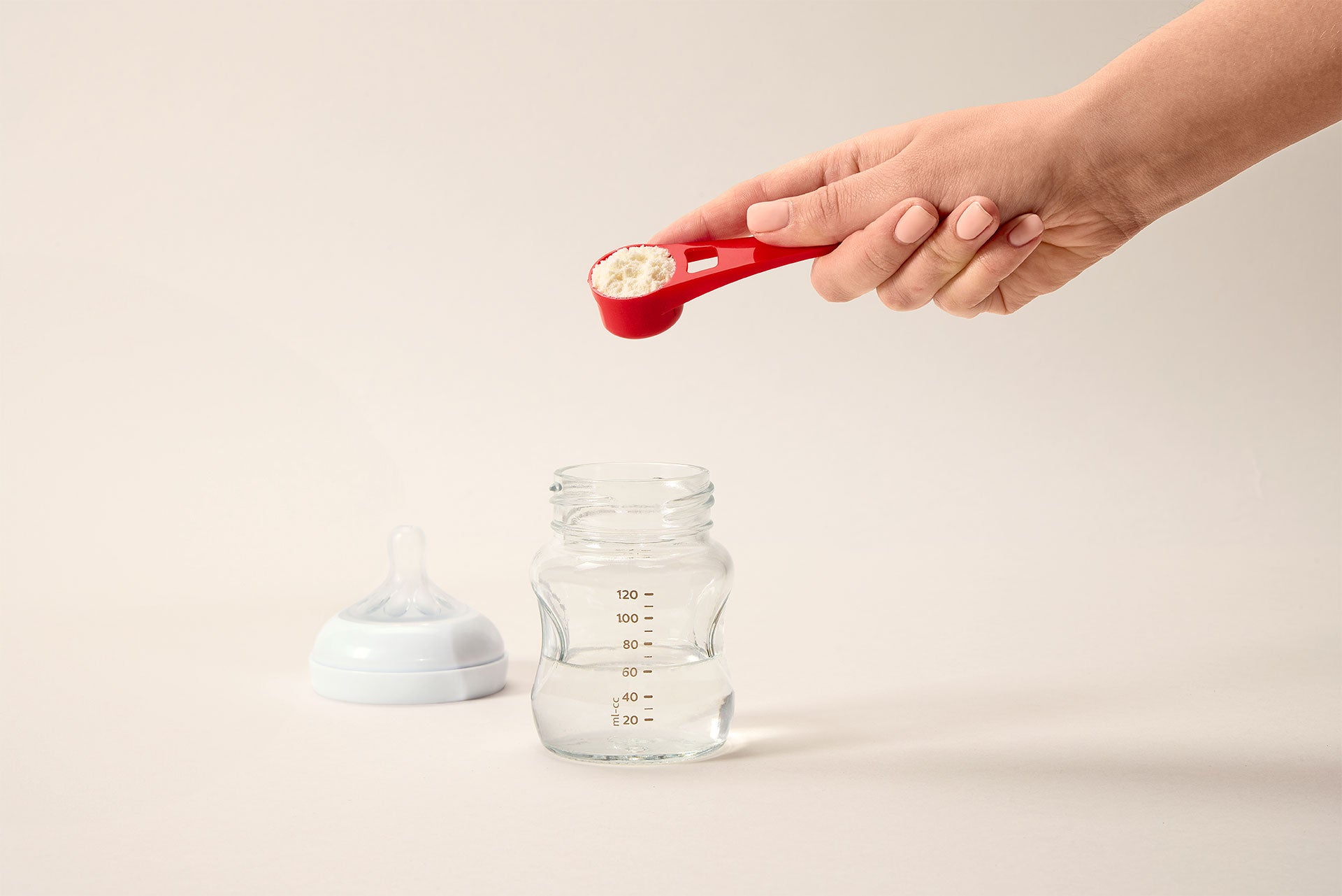 A red Niuriss scoop containing powdered formula, ready to mix with the water in the baby bottle below it.