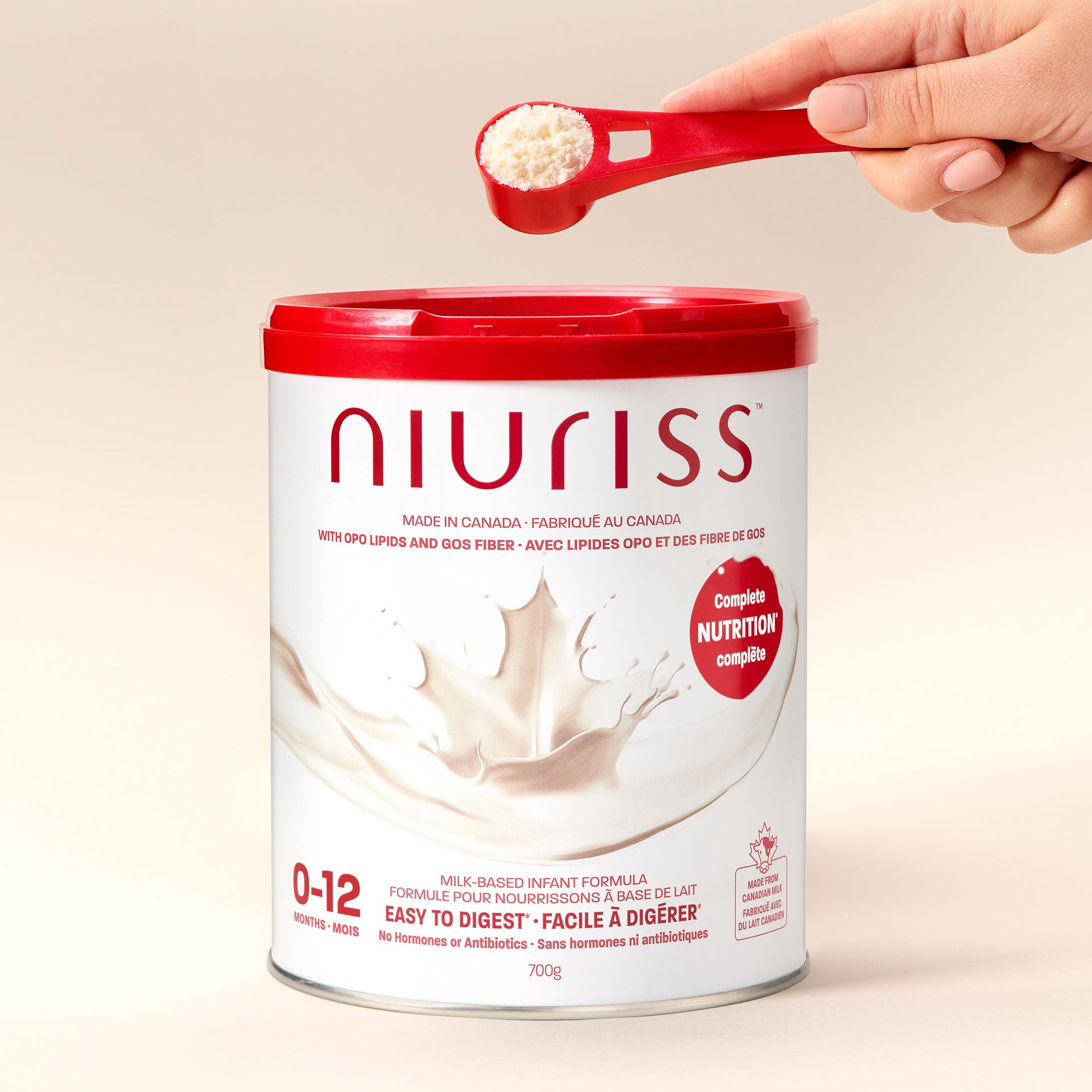 A parent scoops the powder from a can of Niuriss Infant Formula with the red Niuriss measuring scoop.