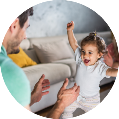 parents playing with their toddler as she takes her first steps.