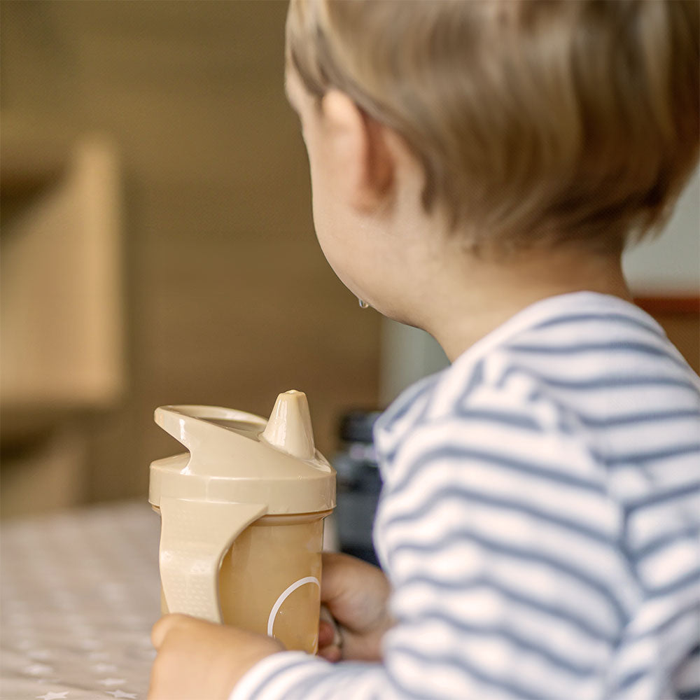 318 A W a day ago  A toddler sits upright facing away from the camera, holding a large sippy cup filled with toddler formula.