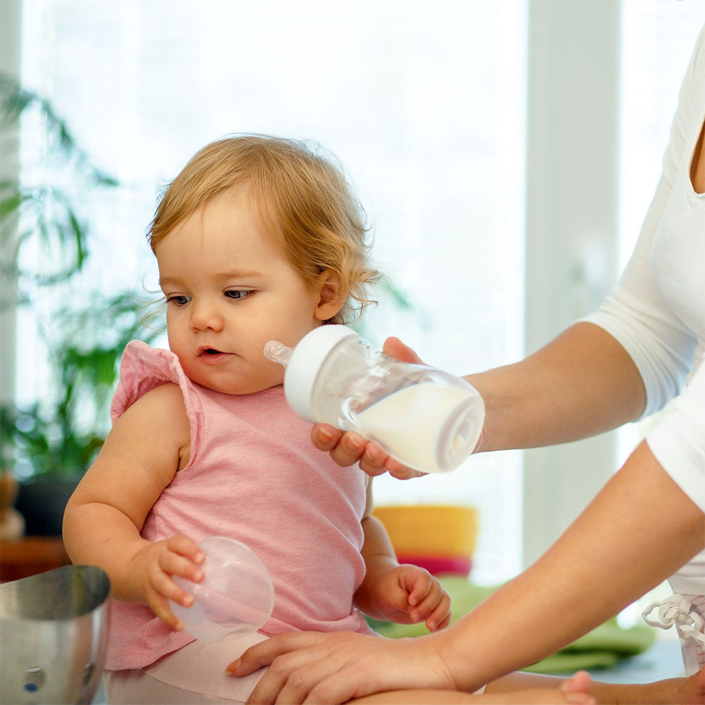 A baby turns away from the bottle of formula her mom presents, demonstrating one of her fullness cues.