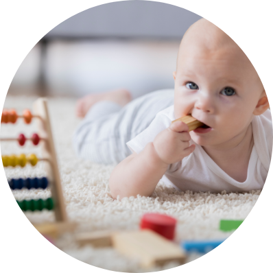 A baby lies on a soft rug during playtime, surrounded by toys as he chews on a block.