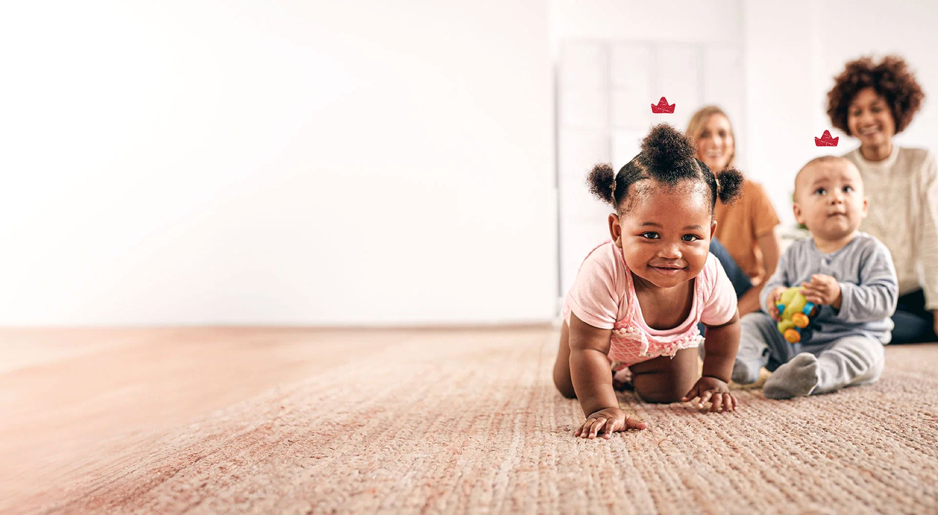 Two babies with Niuriss crowns hovering above their heads on a rug at playtime. Their mother smile in the background.