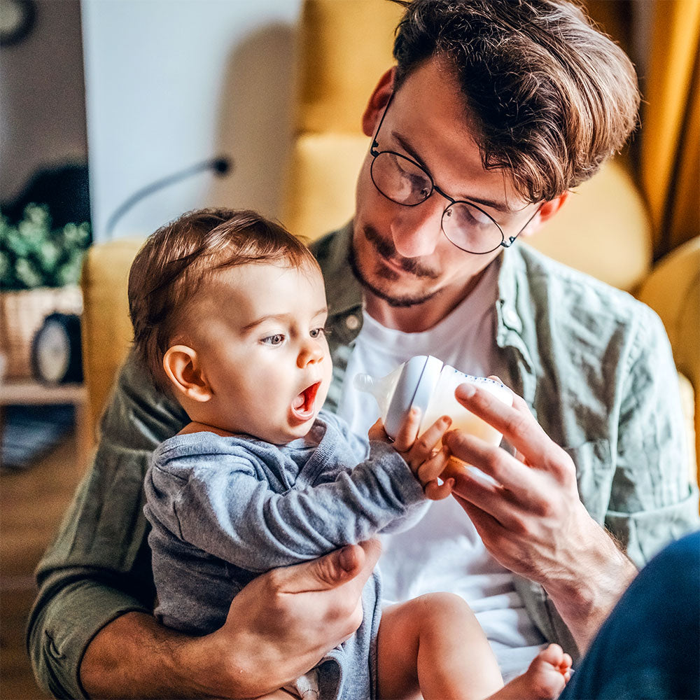 A hungry baby holds his formula bottle with both hands, demonstrating one his feeding cues. 