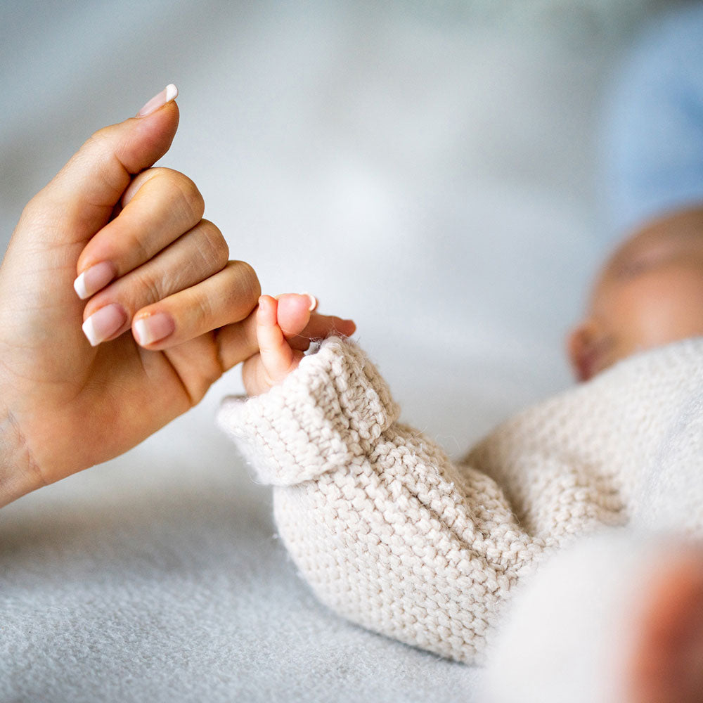 A baby holds its mother's pinky as it lies in its crib.