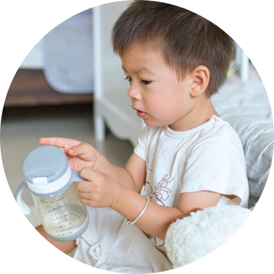 A toddler sits upright and holds a near-empty sippy cup of formula, representing responsible nourishment.