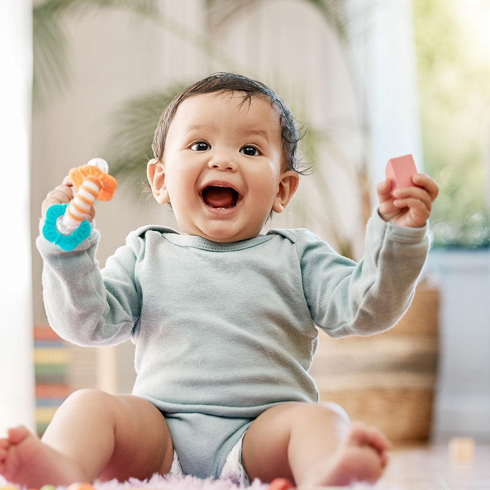 A smiling infant holds a toy in each hand, showing formula feeding's positive role in nourishing babies.